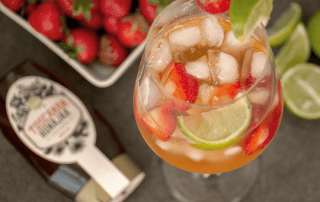 Raikas mansikka-Rooibos-jäätee lasissa, koristeltu limellä ja mansikoilla.