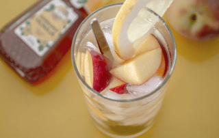 Persikka-kamomilla-jäätee lasissa, sitruunaviipale ja hunajaa.