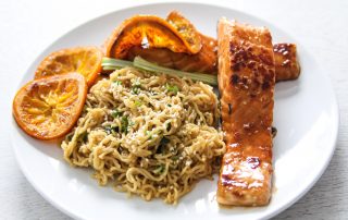 Appelsiinimarinoitu lohi ja valkosipulinuudelit, hunajaiset appelsiiniviipaleet ja tuoreita yrttejä.