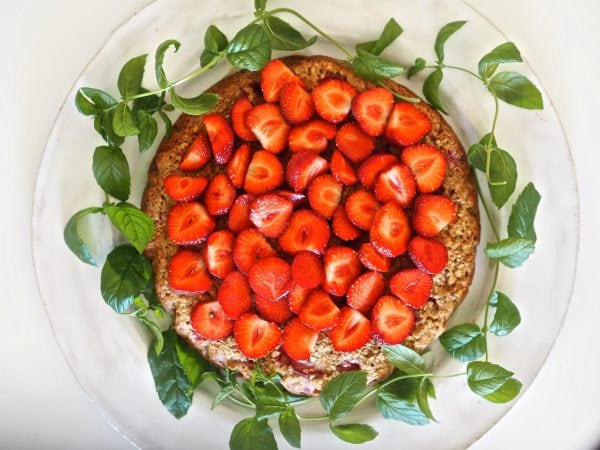 Hunajainen mansikkakakku, koristeltu tuoreilla mansikoilla ja vihreillä lehtikuvioilla.