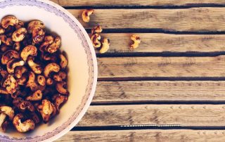 Hunajaiset pähkinät lautasella ja puulautasen pinnalla.